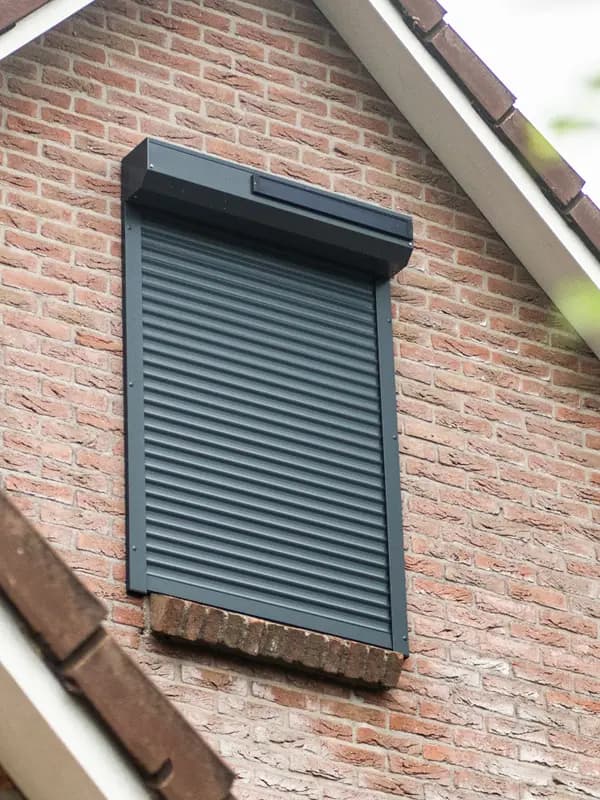 Antraciet rolluik op een raam in een bakstenen gevel