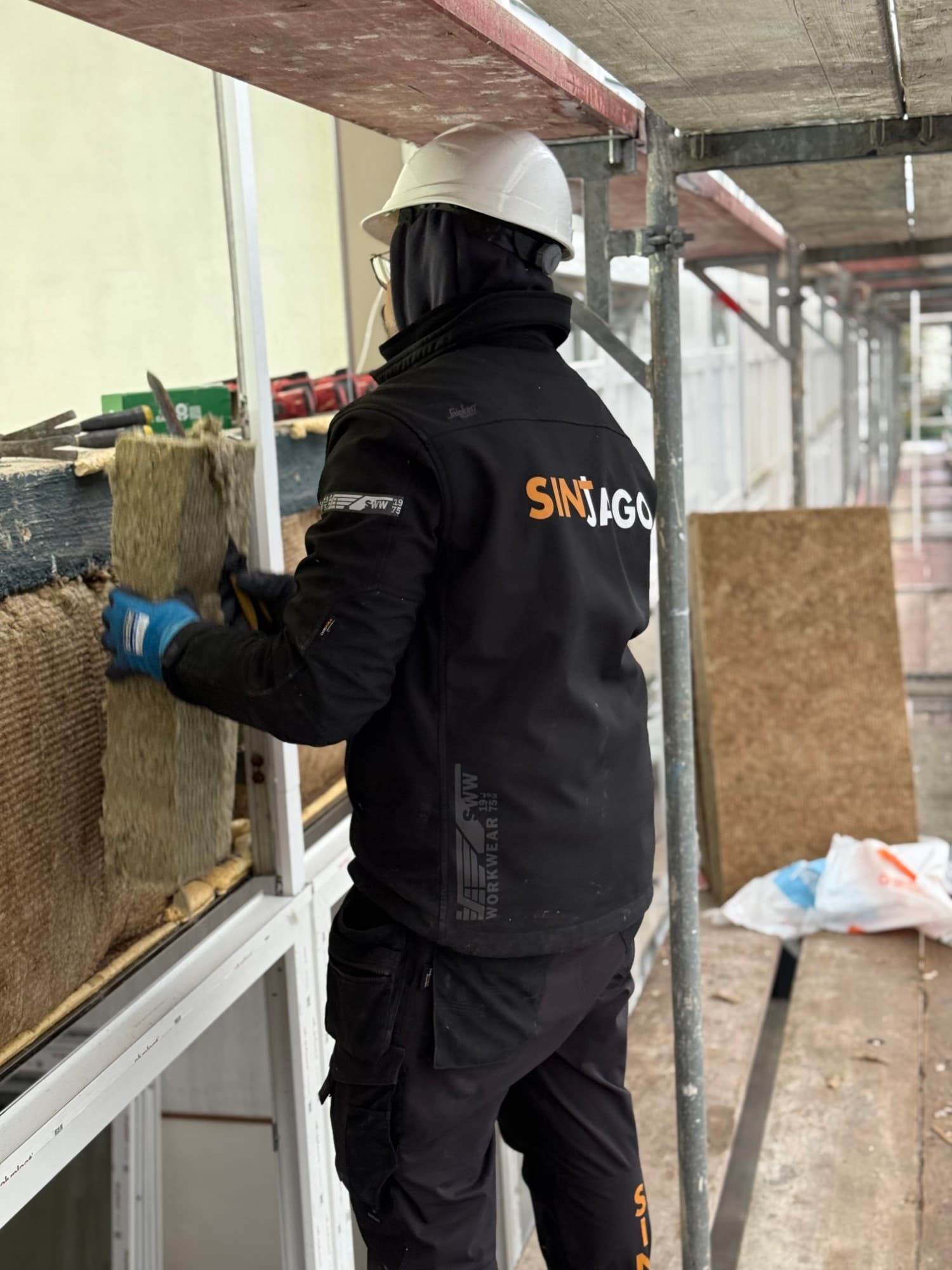 Een monteur van Sintjago Kozijnen met helm en bedrijfsjas plaatst een vliesgevel op de steiger